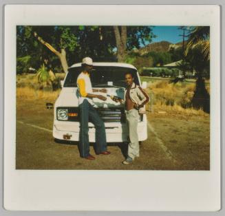 [Two men in front of van, man on right holding bottle of alchohol, man on left with cigarette in mouth]
