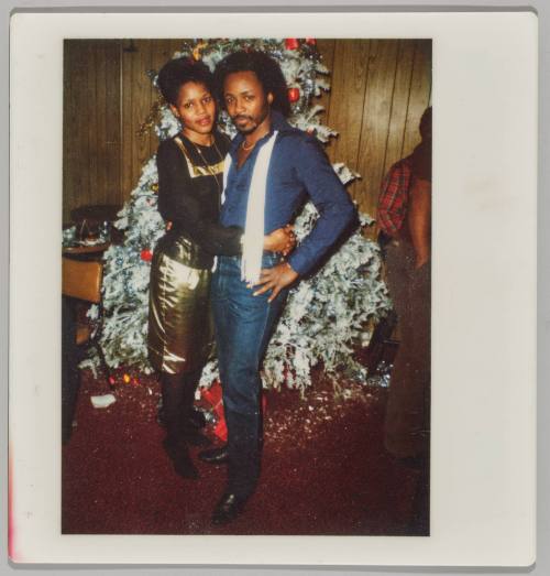 [Man and woman dressed formally embracing in front of Christmas tree]
