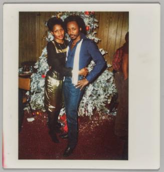 [Man and woman dressed formally embracing in front of Christmas tree]
