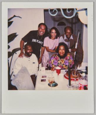 [Three men and two women at dinner party, man on left holding flute]
