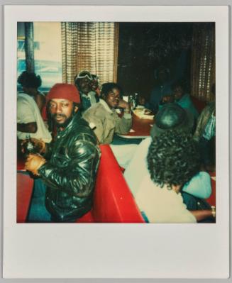 [Men in diner, man in front drinking bottled beverage]
