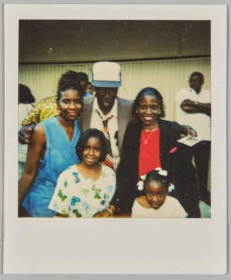 [Two women, man, two girls posing, man holding Polaroid in hand]
