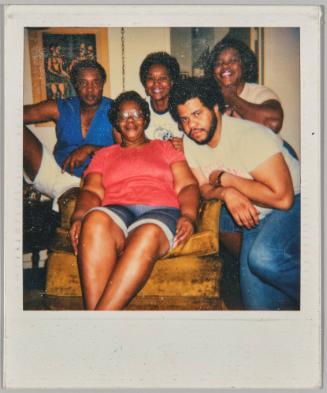 [Four women and a man seated around an armchair]
