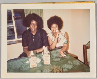 [Two women at table with bottles of gin, one woman smoking holding bottle up to mouth]
