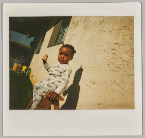 [Toddler in floral onesie sitting on wooden bench outside]
