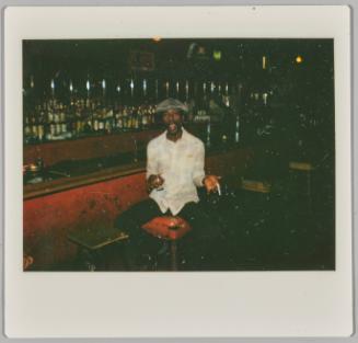 [Young man on seated at bar holding cigarette and glass with mouth open]
