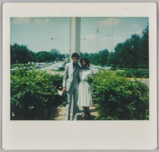 [Adolescent boy and girl dressed formally standing in front of parking lot]
