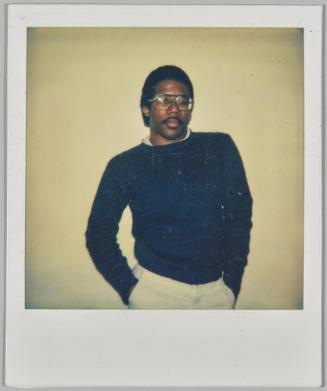 [Man with large glasses posing with hands in pockets]
