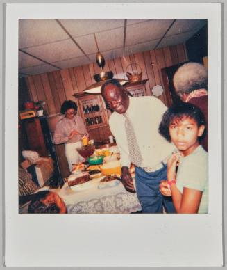 [Man, woman and child in dining room with large meal displayed on table]
