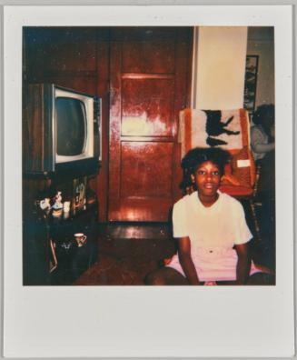 [Girl sitting on ground in wood panelled living room next to television]
