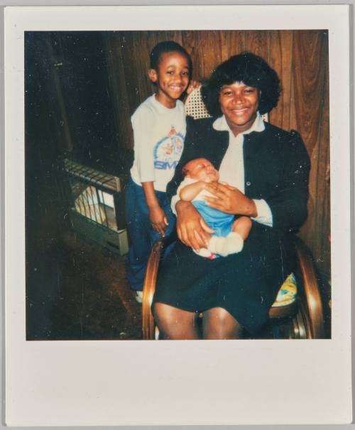 [Woman in rocking chair holding baby with boy at her side]
