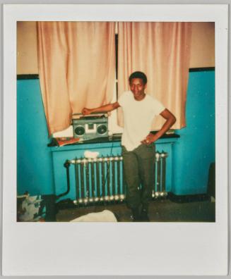 [Adolescent man holding radio beside pink curtains]
