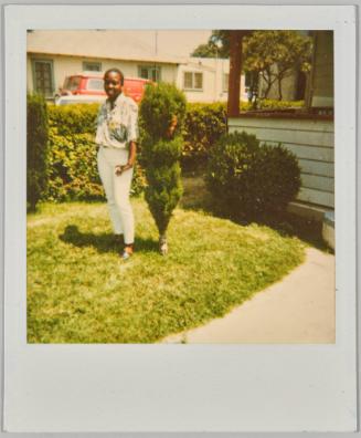 [Woman standing beside small tree on lawn]
