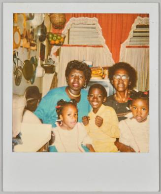 [Two women, two girls and one boy sitting in kitchen with appliances hung on wall]
