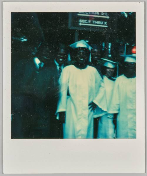 [Seven young adults in white and black graduation robes]
