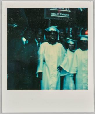 [Seven young adults in white and black graduation robes]
