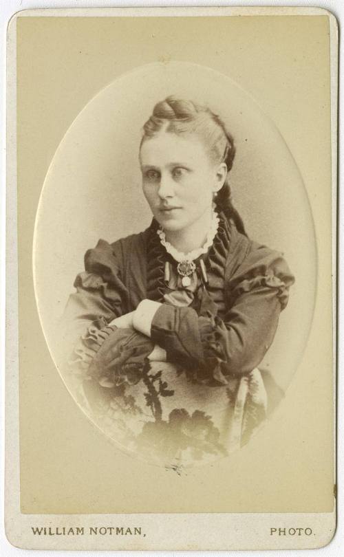 [Young woman sitting with arms folded over the back of a chair]