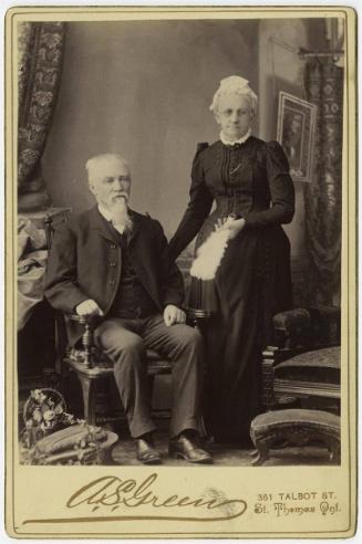 [Older couple, man seated and woman standing]