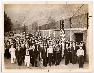 A Large Group of People Walking on a Street and Holding a Large American Flag