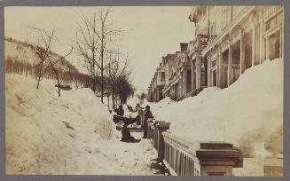 [People standing between large snowbanks on street and in front of houses]