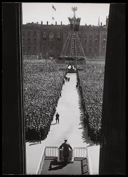 Looking down on Hitler addressing a crowd of thousands. Sign in foreground.
