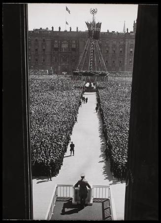 Looking down on Hitler addressing a crowd of thousands. Sign in foreground.