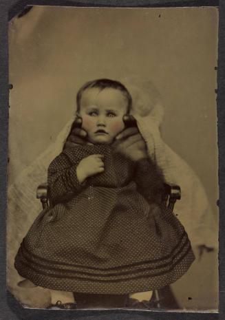 Portrait of young child in polka-dot dress (seated on chair with hands supporting face)