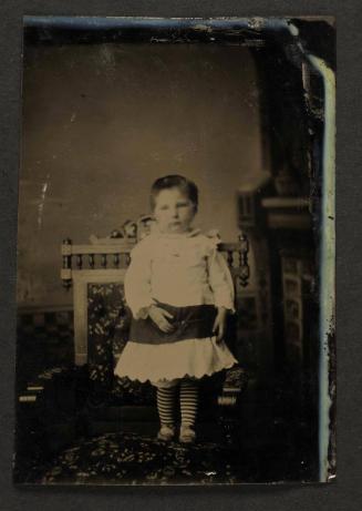 Unknown sitter [portrait of a standing infant in striped tights]