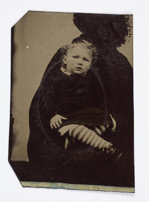 Portrait of young child with striped stockings (seated on lap supported by defaced figure)
