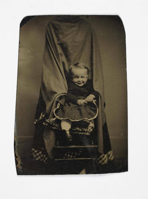 Portrait of young child (seated in front of shrouded figure)