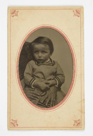 Portrait of a young boy (seated on lap of cropped figure)