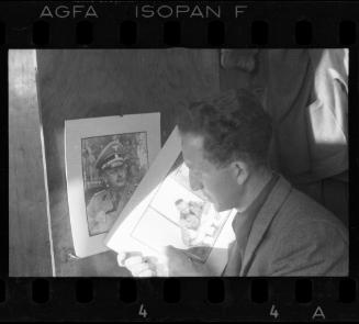 Mendel Grossman, holding a portrait of a German administrator, beside a portrait of a German officer