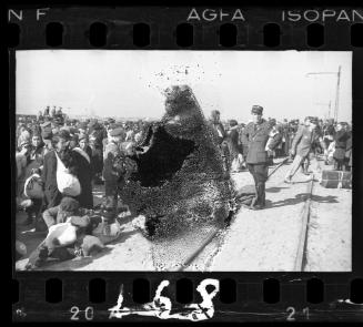 Jewish police and residents gathered in the street beside a railroad track, awaiting deportation