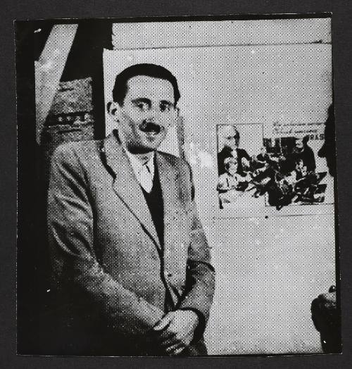 Henryk Ross standing beside photomontage promoting factory production in the ghetto