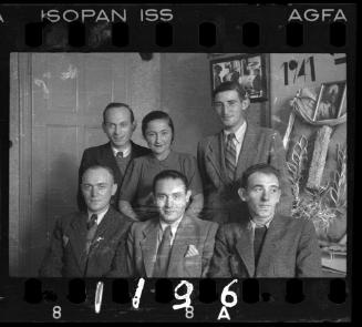 Administrators of the Holzwollefabrik workshop ("ressort") beside a commemorative display, with a portrait of Mordechai Chaim Rumkowski