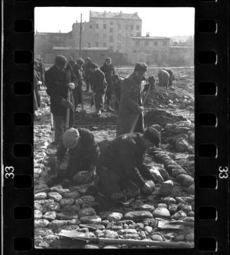 Workers laying [or removing?] stones on a street in the ghetto