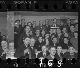 Large group of residents at a reception in the ghetto; man holding a framed award in the back
