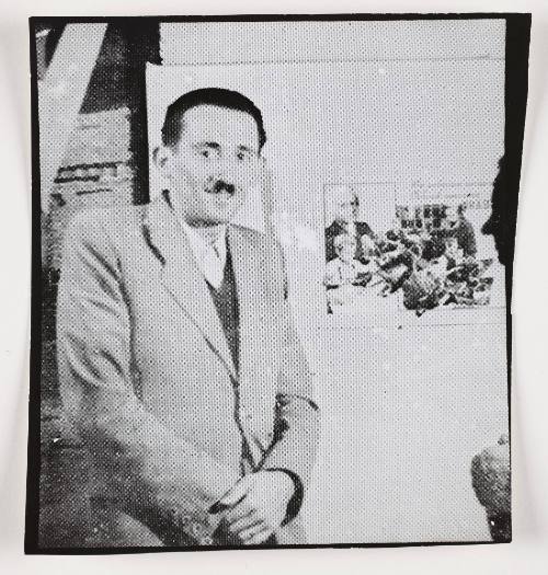 Henryk Ross standing beside photomontage promoting factory production in the ghetto