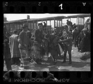 Two Jewish policemen holding elderly man in front of deportation tram