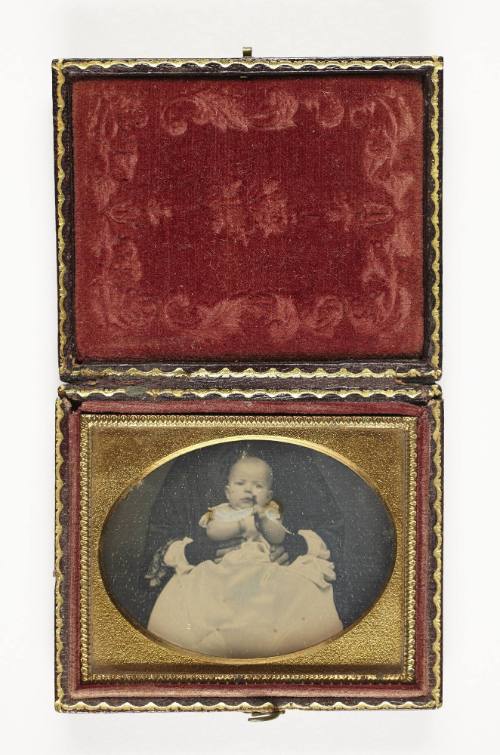 Portrait of baby in white dress (seated on lap)