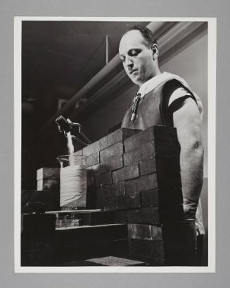 Safeguarding Atomic Workers: A lead brick wall, long-handled tongs, rubber floves and abron, and a radiation counter protect the health of a worker conducting radio-isotope research