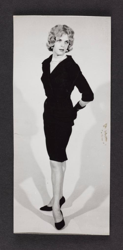 [Donna (Buff/Cynthia) in a dark dress, hands behind back, photo studio]
