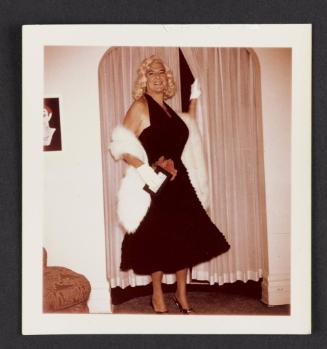 [Blonde in a black dress and white fur shawl, location unknown]
