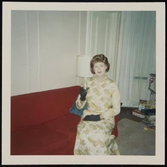 [Blonde in a gold dress, sitting on a red couch with a drink, location unknown]
